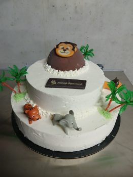 Twee-laags witte taart met jungle thema decoraties, aapje bovenop, olifant en tijger figuren, palmbomen en "Hartelijk Gefelic